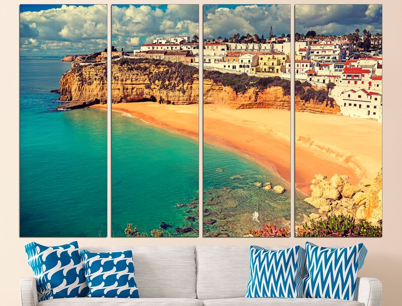 May include: A panoramic view of a coastal town in Portugal. The image shows a white-washed town built on a cliff overlooking a sandy beach and turquoise water. The sky is blue with white clouds.