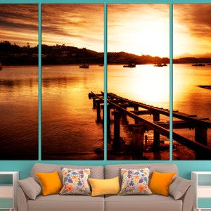 May include: A sunset over a body of water with a wooden pier extending into the water. The sky is a vibrant orange and yellow, and the water is a calm, reflective surface.