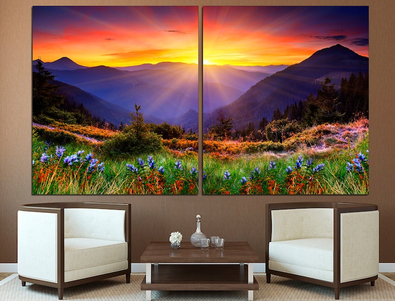 May include: A split canvas print of a mountain landscape with a vibrant sunset sky. The foreground features a field of wildflowers in shades of purple, green, and orange. The mountains are layered in shades of blue and purple, with a golden glow from the setting sun.