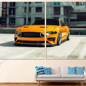 May include: A bright yellow Ford Mustang sports car parked in a concrete car park. The car is facing the camera and has a black grille and black wheels.