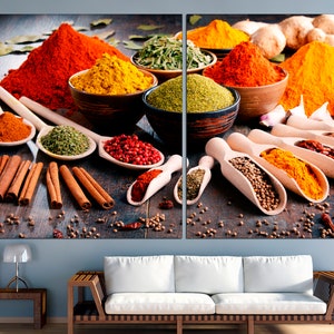 May include: A variety of spices in bowls and spoons, including red chili powder, turmeric, coriander, and cinnamon sticks. The spices are arranged on a wooden surface.