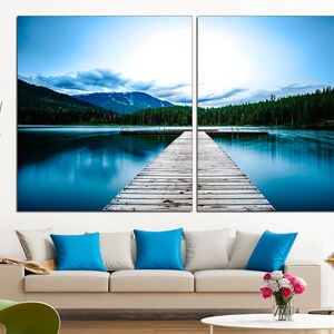 May include: A split canvas print of a wooden dock extending into a still blue lake with a mountain range in the background.