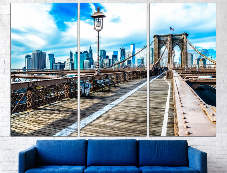 May include: A panoramic view of the Brooklyn Bridge in New York City. The bridge is a suspension bridge with a wooden walkway and a view of the city skyline in the background. The sky is blue with white clouds.