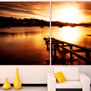 May include: A sunset over a body of water with a wooden pier extending into the water. The sky is a vibrant orange and yellow, and the water is a deep blue.