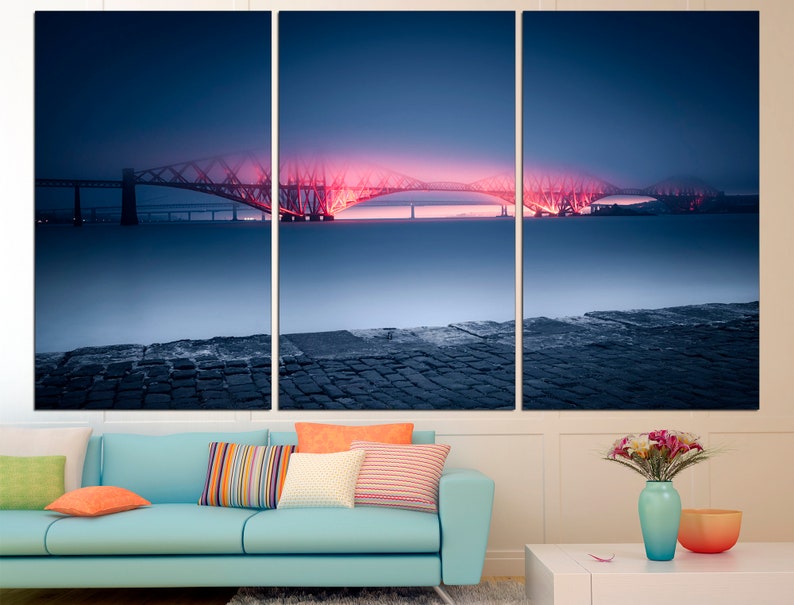 May include: A three-panel canvas print featuring a bridge lit up in pink and red against a dark blue sky. The bridge is reflected in the water below, which is covered in a light fog. The bottom of the image shows a stone walkway.