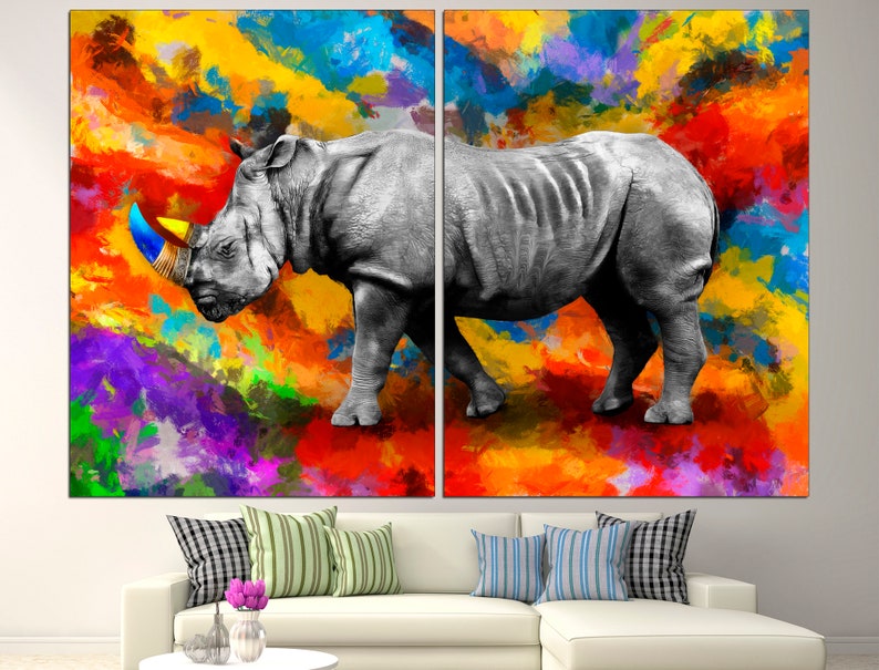 May include: A black and white rhinoceros with a blue and yellow horn stands on a colorful abstract background. The background is a mix of red, orange, yellow, purple, and blue.