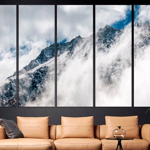 Puede incluir: Una vista panor&aacute;mica de un pico de monta&ntilde;a cubierto de nieve parcialmente oscurecido por las nubes. La monta&ntilde;a es de color gris oscuro con nieve blanca en la cima y los lados. Las nubes son blancas y esponjosas, y se mueven a trav&eacute;s del cielo. El cielo es de color azul claro.
