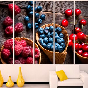 May include: A close-up of three waffle cones filled with fresh fruit. The cones are filled with blueberries, raspberries, and cherries. The fruit is arranged in a visually appealing way, with the blueberries in the center of the cones and the raspberries and cherries surrounding them. The cones are sitting on a wooden surface.