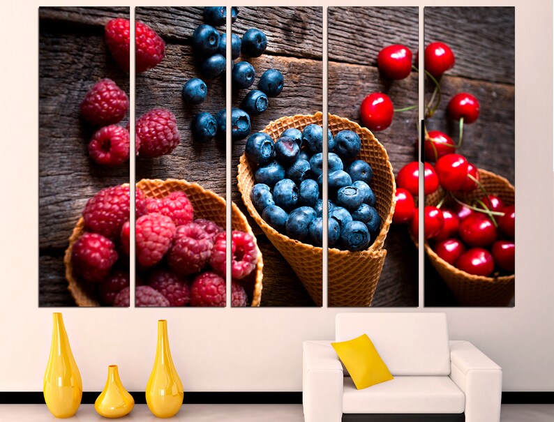 May include: A close-up of three waffle cones filled with fresh fruit. The cones are filled with blueberries, raspberries, and cherries. The fruit is arranged in a visually appealing way, with the blueberries in the center of the cones and the raspberries and cherries surrounding them. The cones are sitting on a wooden surface.
