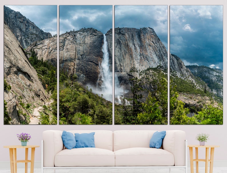 May include: A panoramic view of a waterfall cascading down a rocky cliff face in Yosemite National Park. Lush green trees and a cloudy sky complete the scene.