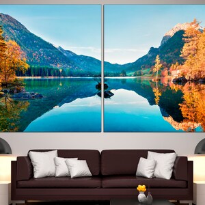May include: A panoramic view of a lake surrounded by mountains with fall foliage reflected in the water.