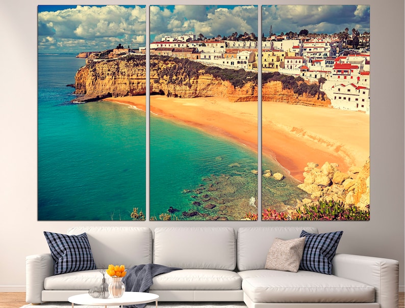 May include: A panoramic view of a coastal town in Portugal. The image shows white buildings perched on a cliff overlooking a sandy beach and turquoise water. The sky is blue with white clouds.