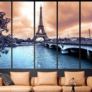 May include: A panoramic view of the Eiffel Tower in Paris, France. The tower is in the center of the image, with the Seine River and a bridge in the foreground. The sky is a soft orange and pink, with clouds.