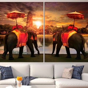 May include: Two elephants adorned with red and gold fabric walk side-by-side in front of a temple at sunset. Each elephant is carrying a red and gold canopy.