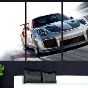 May include: A silver grey Porsche 911 GT3 RS sports car speeding on a race track. The car has a black stripe down the center of the hood and black wheels.