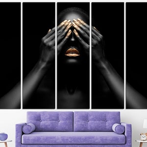 May include: A person with black skin and gold makeup covers their eyes with their hands. The background is black.