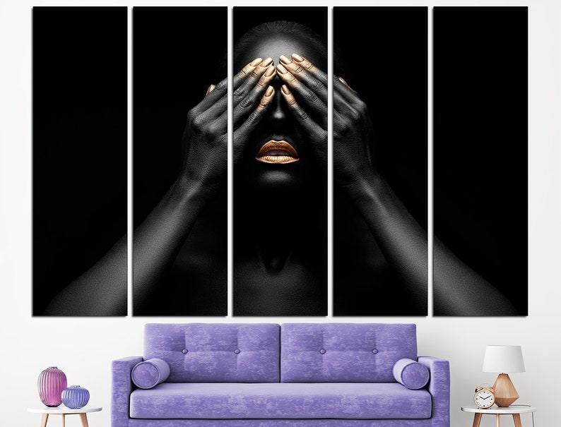 May include: A person with black skin and gold makeup covers their eyes with their hands. The background is black.