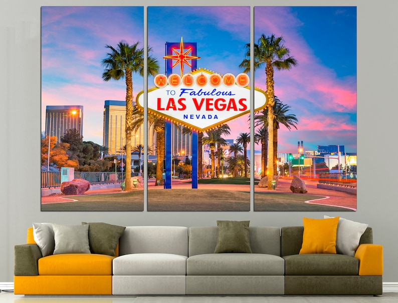May include: A triptych canvas print featuring the iconic "Welcome to Fabulous Las Vegas Nevada" sign at dusk. The sign is illuminated against a backdrop of palm trees, buildings, and a vibrant sky. The artwork is displayed above a modern sofa.