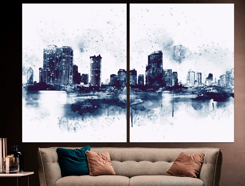May include: A watercolor painting of a city skyline in shades of blue and white. The buildings are silhouetted against a white background, and there are splashes of blue paint throughout the image.