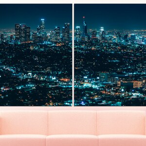Puede incluir: Una vista panor&aacute;mica nocturna de un horizonte urbano con edificios altos iluminados por luces. La ciudad se extiende hacia abajo, con muchos edificios m&aacute;s peque&ntilde;os y calles visibles. El cielo es azul oscuro y las luces crean un brillo c&aacute;lido.