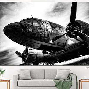 May include: A black and white photograph of a vintage airplane with a propeller. The airplane is sitting on the ground with the propeller facing the camera. The airplane is weathered and has a lot of detail.
