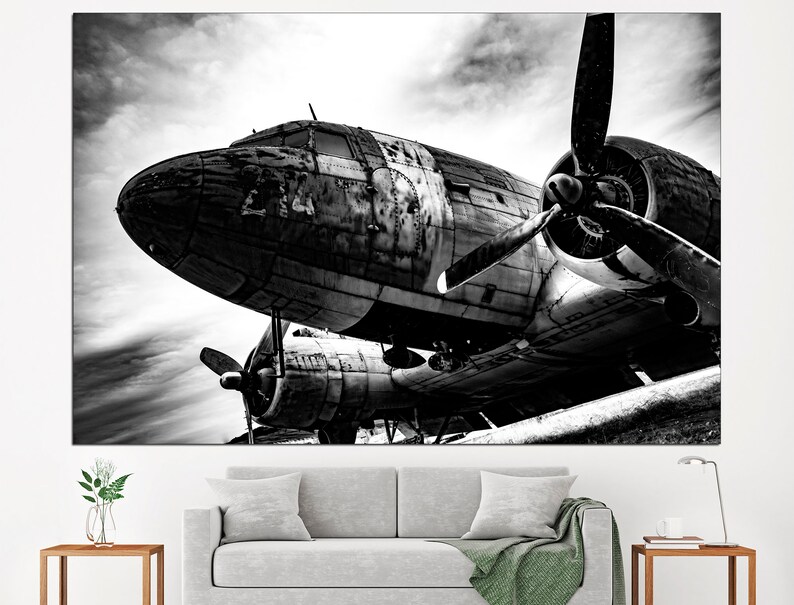 May include: A black and white photograph of a vintage airplane with a propeller. The airplane is sitting on the ground with the propeller facing the camera. The airplane is weathered and has a lot of detail.