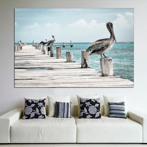 May include: A photograph of a wooden pier extending into a turquoise ocean. A pelican stands on a wooden post at the end of the pier. Several other pelicans are perched on posts in the distance.