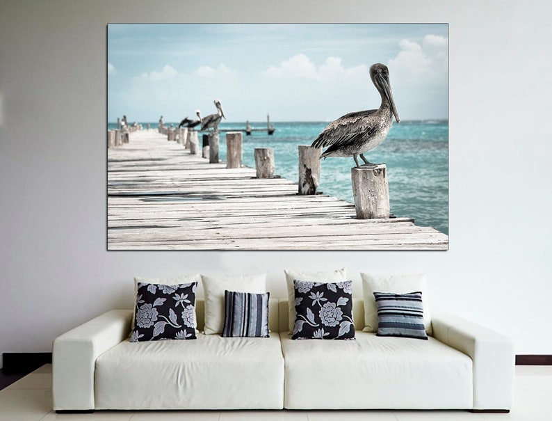 May include: A photograph of a wooden pier extending into a turquoise ocean. A pelican stands on a wooden post at the end of the pier. Several other pelicans are perched on posts in the distance.