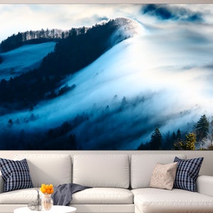May include: A panoramic view of a misty forest with rolling hills and a blue sky. The fog is thick and white, and the trees are dark green. The image is taken from a high vantage point, looking down on the forest.