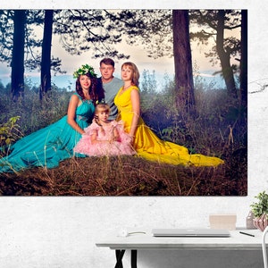 May include: A family of four poses in a forest setting. The mother wears a turquoise dress, the father wears a blue shirt, the daughter wears a yellow dress, and the young girl wears a pink dress. The family is surrounded by green trees and foliage.