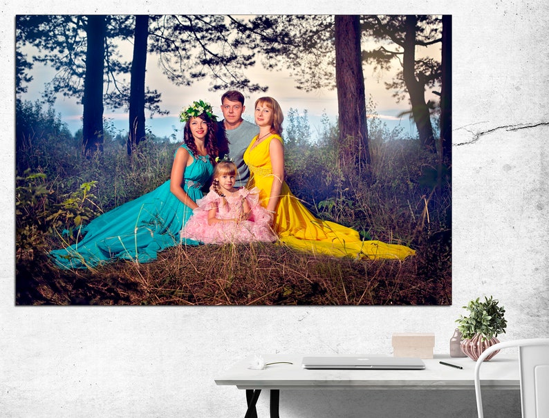 May include: A family of four poses in a forest setting. The mother wears a turquoise dress, the father wears a blue shirt, the daughter wears a yellow dress, and the young girl wears a pink dress. The family is surrounded by green trees and foliage.