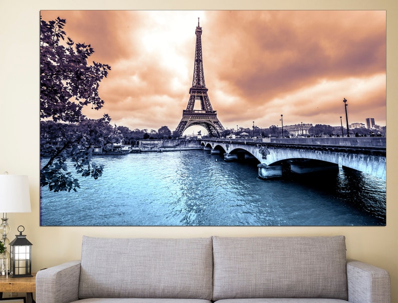 May include: A black and white photograph of the Eiffel Tower in Paris, France. The tower is in the background, with a bridge and river in the foreground. The sky is a light orange color.