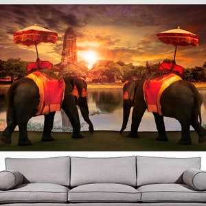 May include: Two elephants adorned with red and gold fabric walk side-by-side in front of a temple with a sunset in the background.