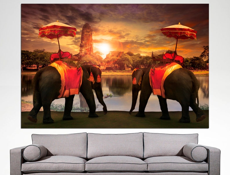 May include: Two elephants adorned with red and gold fabric walk side-by-side in front of a temple with a sunset in the background.