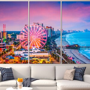 May include: A panoramic view of a coastal city with a Ferris wheel in the foreground. The city skyline is visible in the distance, with a beach and ocean in the background. The sky is a vibrant pink and purple, with a soft glow of light reflecting off the water.