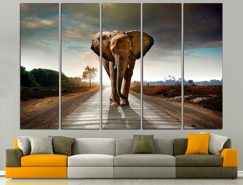 May include: A large elephant walks down a dirt road in a multi-panel canvas art print. The elephant is brown and has large ears. The road is surrounded by trees and bushes. The sky is cloudy and the sun is setting.