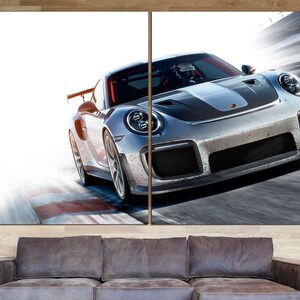 May include: A silver and black sports car speeding on a race track. The car has a black stripe down the hood and a large wing on the back.