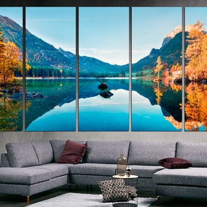 May include: A panoramic landscape photograph of a lake surrounded by mountains and trees. The lake is reflecting the mountains and trees, creating a mirror-like effect. The trees are in autumn colors, with shades of yellow, orange, and red.