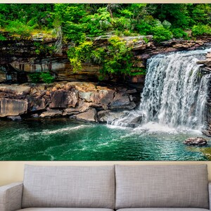 May include: A cascading waterfall flows over moss-covered rocks into a clear, green pool. Lush greenery surrounds the waterfall, creating a serene and picturesque scene.