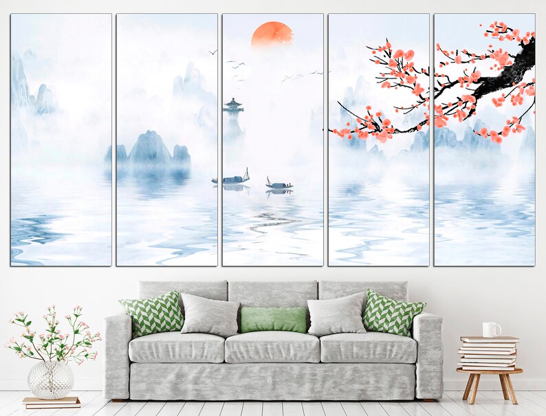 May include: A multi-panel canvas print depicting a serene landscape with misty mountains, a calm lake, and a traditional Chinese building. The scene is painted in soft blue and white tones, with a touch of orange for the rising sun. A delicate branch of pink blossoms adds a touch of color to the composition.