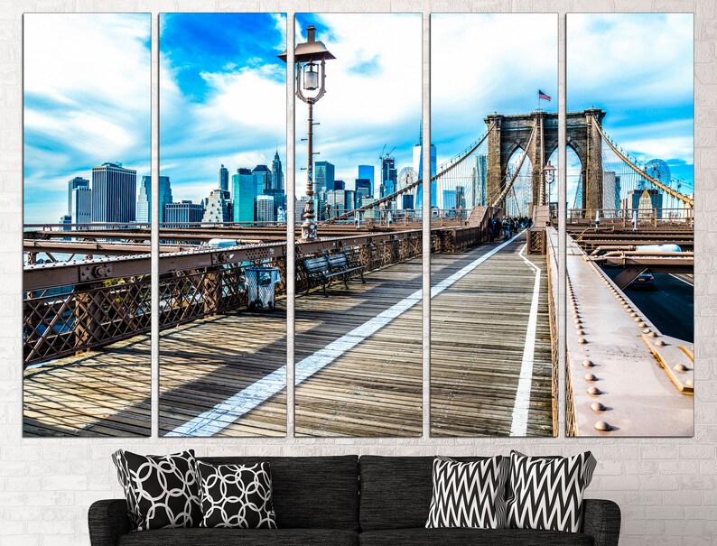 May include: A panoramic view of the Brooklyn Bridge in New York City. The bridge is a suspension bridge with a wooden walkway and a view of the city skyline in the background. The sky is blue with white clouds.