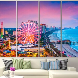 May include: A panoramic view of a city skyline with a Ferris wheel in the foreground. The city is located on a beach with a pier extending into the ocean. The sky is a vibrant pink and purple.