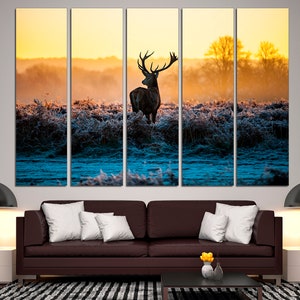 May include: A multi-panel canvas print depicting a silhouette of a deer standing in a field at sunrise. The deer is facing away from the viewer, with its antlers visible. The background is a soft, golden light, with a hint of blue in the distance.