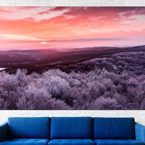 May include: A panoramic view of a forest covered in frost with a pink and orange sunset in the background.