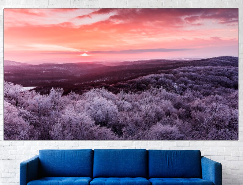May include: A panoramic view of a forest covered in frost with a pink and orange sunset in the background.