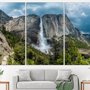 May include: A panoramic view of a waterfall cascading down a rocky cliff face in Yosemite National Park. Lush green trees and a cloudy sky complete the scene.