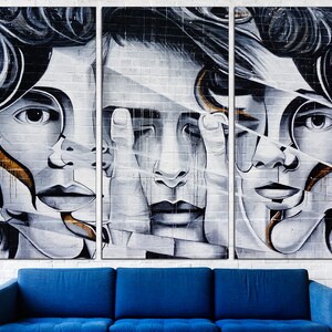 May include: A triptych of three black and white portraits of people with their faces partially obscured by geometric shapes. The portraits are painted on a white brick wall background.