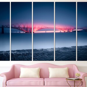 May include: A five-panel canvas print of a bridge lit up in pink and red at night. The bridge is over a body of water and there is a stone walkway in the foreground.