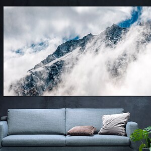 Puede incluir: Un pico de monta&ntilde;a parcialmente oculto por las nubes. La monta&ntilde;a est&aacute; cubierta de nieve y hielo. El cielo es azul con nubes blancas.
