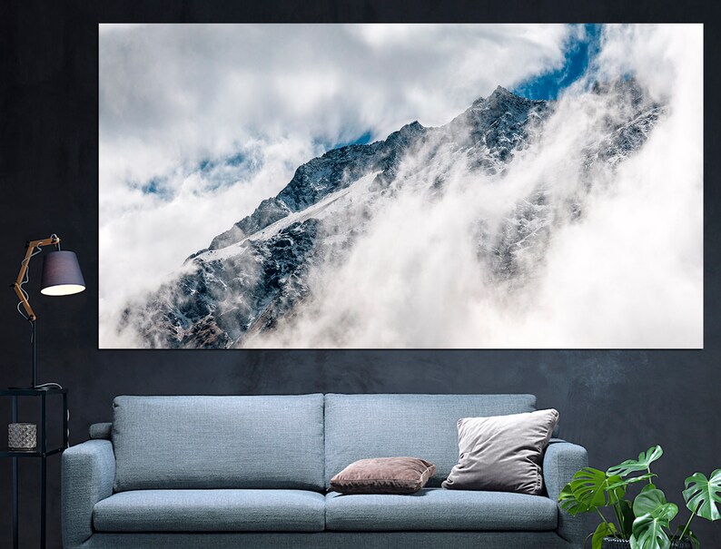 Puede incluir: Un pico de monta&ntilde;a parcialmente oculto por las nubes. La monta&ntilde;a est&aacute; cubierta de nieve y hielo. El cielo es azul con nubes blancas.